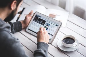 man watching video on website on tablet along with cup of coffee